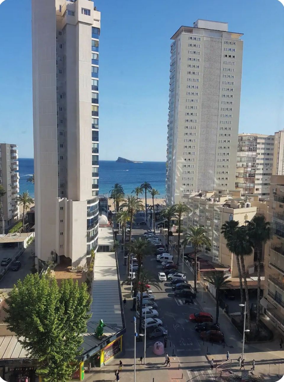 Um edifício alto com vista para o oceano e um estacionamento cheio de carros.