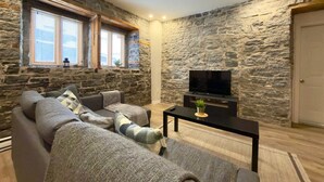A living room with stone walls, a sofa set, a TV, and a small table. - A lovely apartment with Victorian charm (Québec)