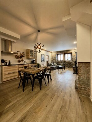 Eine geräumige Küche mit Holzboden, eine Essecke mit einem Holztisch und Stühlen sowie eine Wand mit Steinverkleidung.