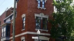 Edifício de tijolos vermelhos com entrada de canto, placa de rua visível e pequena varanda.