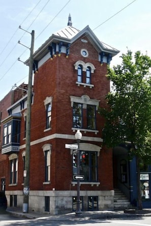 Ein rot Backsteingebäude mit Hauseingang an der Ecke, einem sichtbaren Straßenschild und einem kleinen Vorbereich.