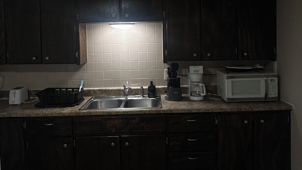 A kitchen with dark cabinets, a tiled backsplash, a sink, a coffee maker, and a microwave. - Home Away From Home II (Amarillo)