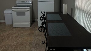 A compact kitchen with a stove, oven, refrigerator, and a dining table with chairs. - Home Away From Home II (Amarillo)