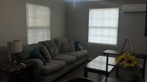 A living room with a ceiling fan, a sofa, a coffee table, and a dining table with a vase of sunflowers. - Home Away From Home II (Amarillo)