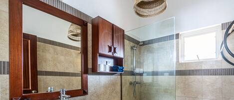 Un baño moderno con ducha de vidrio, tocador de madera con espejo y salpicadero de azulejos.