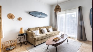 Ein Wohnzimmer mit einem beigen Sofa, einem Couchtisch, einem Korbwäscher und einer hängenden Deckenleuchte.
