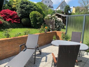 A patio with two chairs and a table, surrounded by a brick wall and a garden with various plants and flowers.