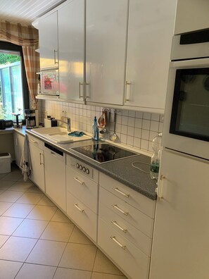 A kitchen with white cabinets, a granite countertop, a built-in oven, and a window with curtains.