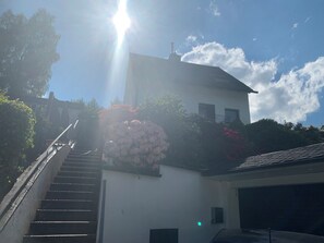 A building with a staircase leading to a garage, surrounded by greenery and a clear sky.