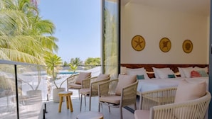 Una habitación de hotel moderna con balcón, mobiliario de mimbre y una cama con muchas almohadas.