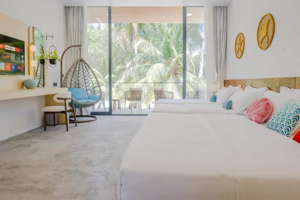 Ein Hotelzimmer mit einem großen Bett, einer Sitzecke mit Sesseln, einem Balkon mit Blick auf Palmen und einem an der Wand befestigten Fernseher.