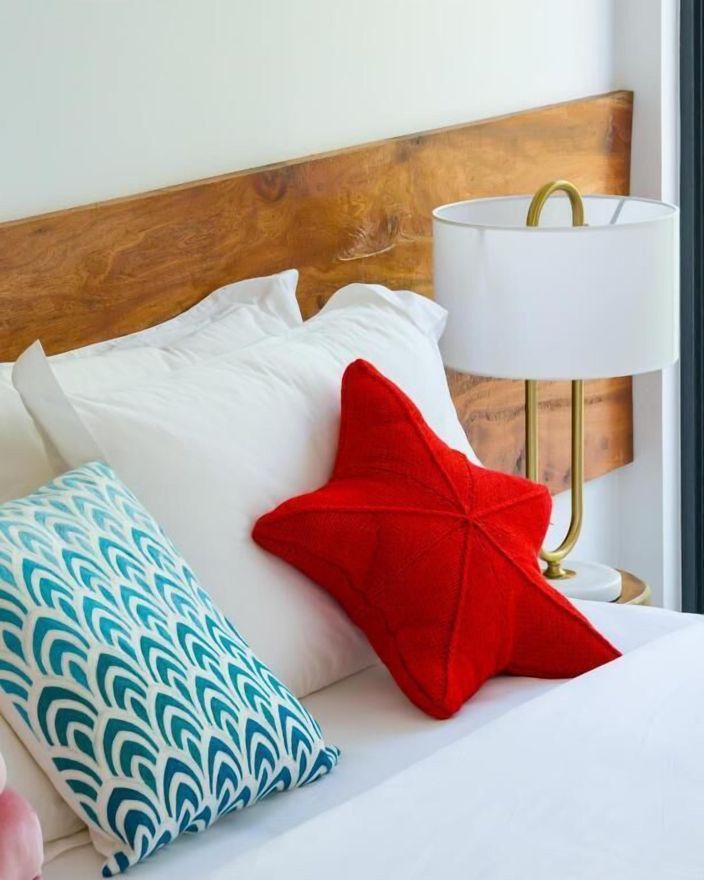 A bed with white bedding, a wooden headboard, and a red star-shaped pillow.