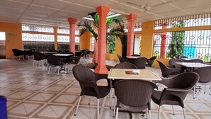 A spacious indoor area with multiple tables and chairs, large windows with metal bars, and a tiled floor.