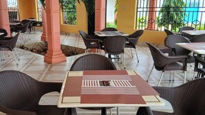 An outdoor café with tiled flooring, wicker furniture, and a view of greenery.