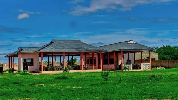 A two-story building with a covered patio area, a small garden, and a clear blue sky.