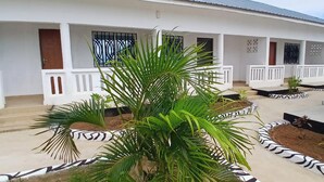 A white building with multiple balconies, a central palm tree, and a patterned garden border.