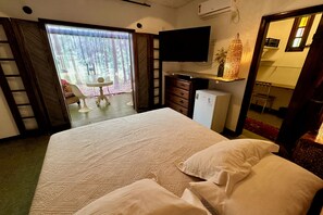 Habitación de hotel con cama, televisor, cómoda, escritorio con silla y puerta corrediza de vidrio que da a un espacio exterior.