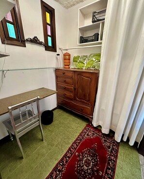Ein Zimmer mit einem Holzkabinett, einer Glasablage, einem gemusterten Teppich und einem Fenster mit Buntglas.