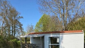 A small white mobile home with a red roof, a porch with a railing, and a grassy yard.