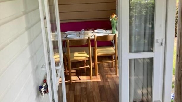 A wooden deck with a dining table and chairs, a door leading inside, and a window with a view.