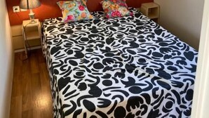 A bedroom with a bed, a nightstand, a lamp, a window with curtains, and a wooden headboard.
