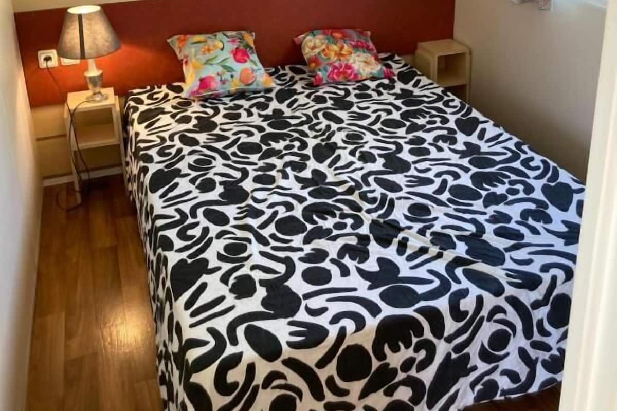 A bedroom with a bed, a nightstand, a lamp, a window with curtains, and a wooden headboard.