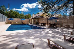 A swimming pool with lounge chairs and umbrellas, surrounded by a fence and trees. - Innsbrook Vacation Condo 36 (Ruidoso)
