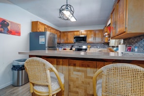 A kitchen with wooden cabinets, a stainless steel refrigerator, a microwave, and a large island with two wicker chairs. - Innsbrook Vacation Condo 36 (Ruidoso)