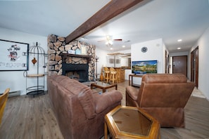 A living room with a stone fireplace, leather sofas, a coffee table, and a television. - Innsbrook Vacation Condo 36 (Ruidoso)