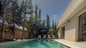 A clear swimming pool with lounge chairs, surrounded by trees and a building with large windows. - Villa Tilelli - Pool & Quiet - 15 minutes from Essaouira (Essaouira)