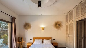 A bedroom with a large bed, wooden headboard, two bedside tables, a wall-mounted light, and a ceiling with a circular design. - Villa Tilelli - Pool & Quiet - 15 minutes from Essaouira (Essaouira)