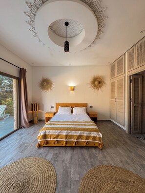 Ein Schlafzimmer mit einem großen Bett, einem Holz-Kopfteil, zwei Nachttischen, einer Wandleuchte und einer Decke mit kreisförmigem Muster.
