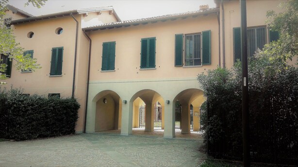 A building with a courtyard, green shutters, and arched walkways.