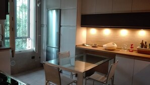 A modern kitchen with a glass dining table, stainless steel appliances, and a brick backsplash.