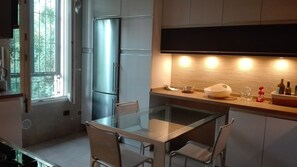 Une cuisine moderne avec une table à manger en verre, des appareils électroménagers en acier inoxydable et un mur de fond en briques.