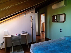 Un dormitorio con una cama, un escritorio con silla, un espejo y una puerta que da a otra habitación.