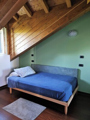 A single bed in a room with a sloped ceiling, a small rug, and a wall-mounted light switch.