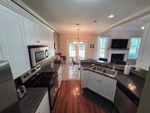 A modern kitchen with white cabinets, a built-in stove, a sink, and a dining area with a chandelier.