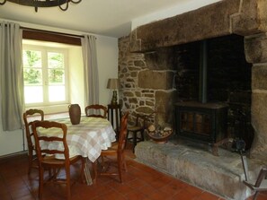 Une pièce avec une cheminée en pierre, une table avec des chaises, une fenêtre avec des rideaux et une lampe.