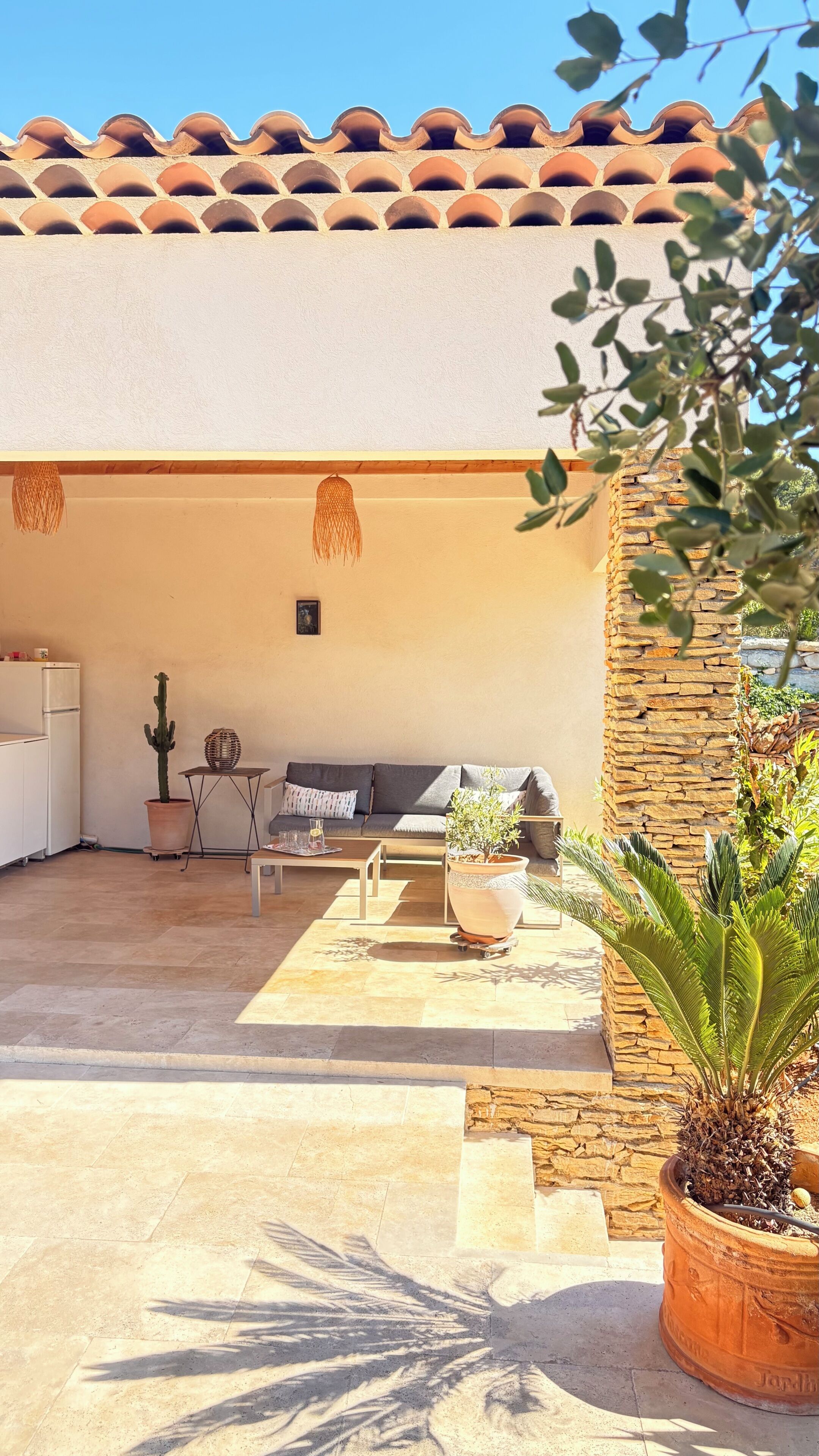 Un patio al aire libre con pared de piedra, zona de estar con sofá y mesa, una planta de cactus y una planta en maceta.
