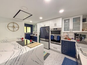 A modern kitchen with white cabinets, a marble countertop, a built-in oven, and a refrigerator. - Designer Waterfront Reno : Master Spa : Weekly Cleaning : 3-Min walk to Beach (Madeira Beach)