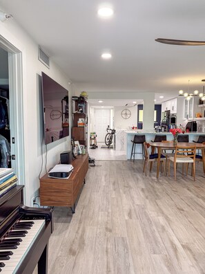 A modern living room with a piano, a wooden cabinet, and a dining area with a table and chairs. - Designer Waterfront Reno : Master Spa : Weekly Cleaning : 3-Min walk to Beach (Madeira Beach)