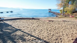 A sandy beach with a pier extending into calm waters, a clear sky, and distant mountains. - Lake Front Resort Unit 31 (Tahoe Vista)