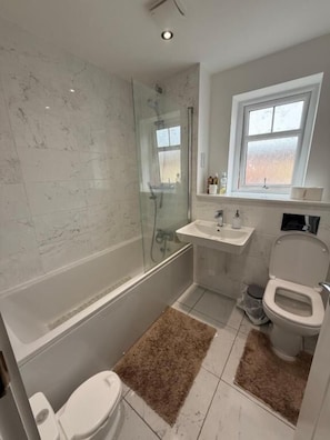 A bathroom with a glass-enclosed shower, a toilet, a sink, and a window.