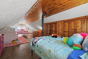 A cozy attic bedroom with a sloped ceiling, wooden walls, a bed with colorful bedding, and a pink rug.