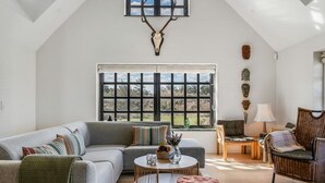 A spacious living area with a high ceiling, a large window, a sofa, a coffee table, a wicker chair, and a wall-mounted deer head. - "Dorit" - 450m from the sea by Interhome (Blokhus)