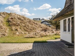 Ein gepflasterter Innenhof mit einem grasbewachsenen Hügel, ein Gebäude mit einem Strohdach und ein moderner Bau im Hintergrund.