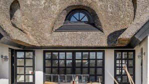 A thatched-roof building with a large window and a table with chairs outside. - "Dorit" - 450m from the sea by Interhome (Blokhus)