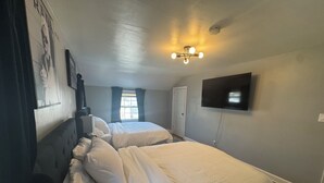 Une chambre avec deux lits, un ventilateur de plafond, une télévision et une fenêtre avec des rideaux.