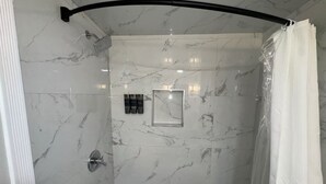 Une salle de bain avec une douche, une baignoire, des murs en marbre, un tableau encadré et un porte-serviettes.